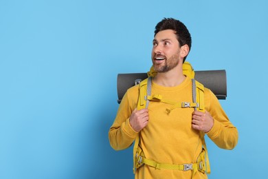 Photo of Happy man with backpack on light blue background, space for text. Active tourism