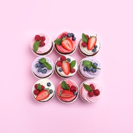 Photo of Different delicious cupcakes with cream and berries on pink background, flat lay