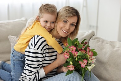 Photo of Little daughter congratulating her mom with Mother`s Day at home. Woman holding bouquet of alstroemeria flowers