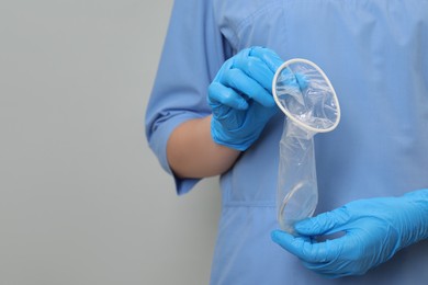 Photo of Doctor with unrolled female condom on light grey background, closeup. Space for text