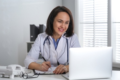 Doctor with headset and laptop consulting patient online in office. Hotline service