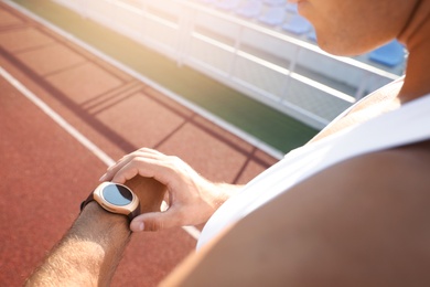 Photo of Man checking fitness tracker after training at stadium, closeup