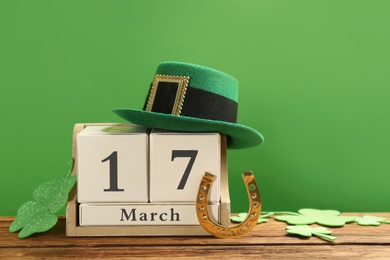 Photo of Composition with leprechaun hat and block calendar on wooden table against green background. St Patrick's Day celebration