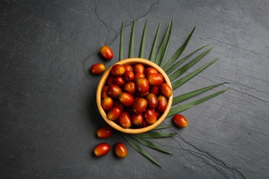 Photo of Palm oil fruits in bowl on black table, flat lay