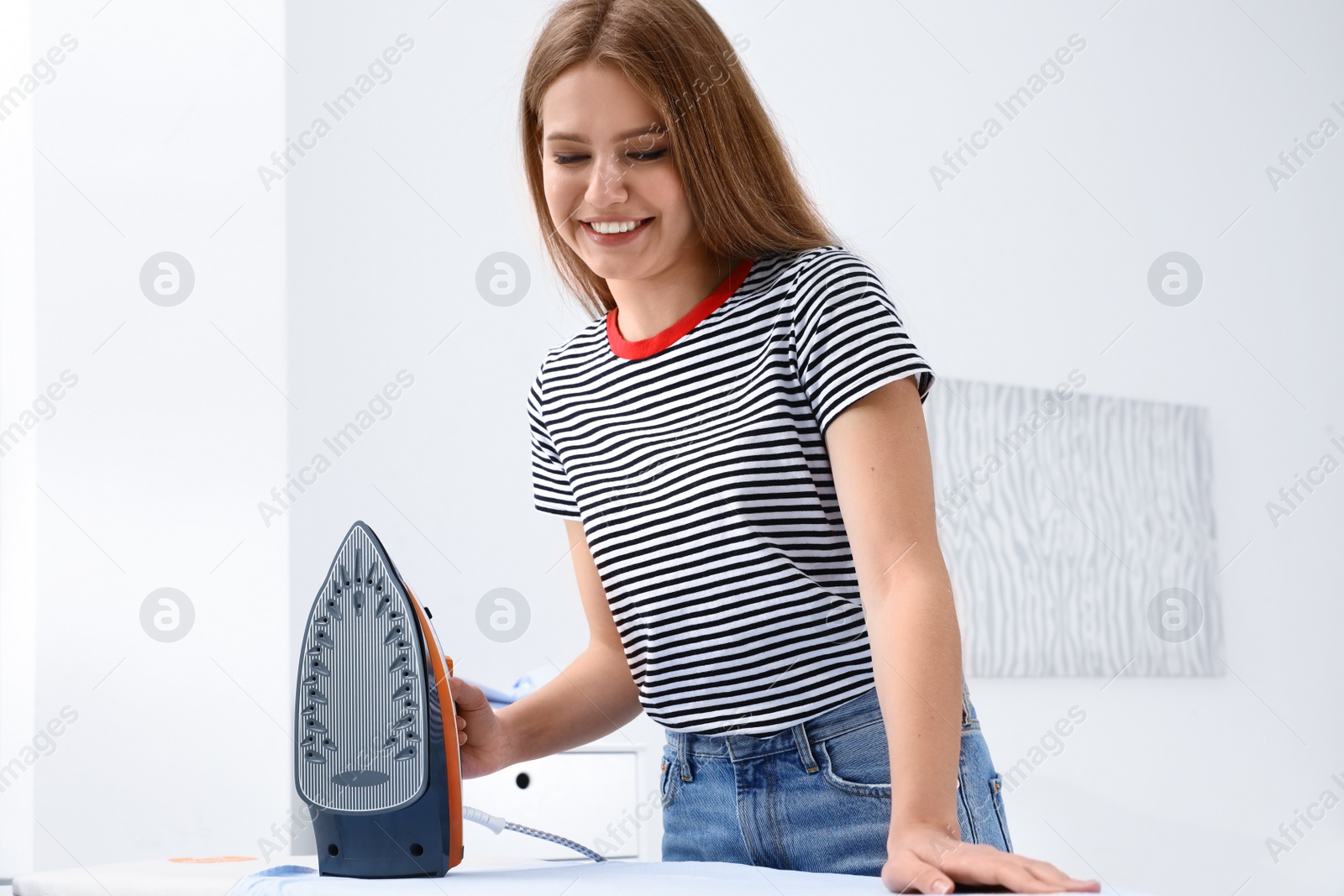 Photo of Young woman ironing clothes on board at home