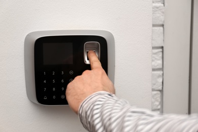 Photo of Man scanning fingerprint on alarm system indoors, closeup