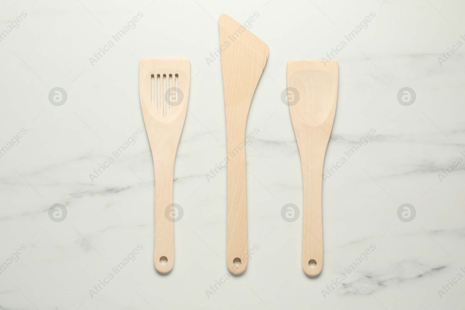 Photo of Different wooden spatulas on white marble table, flat lay