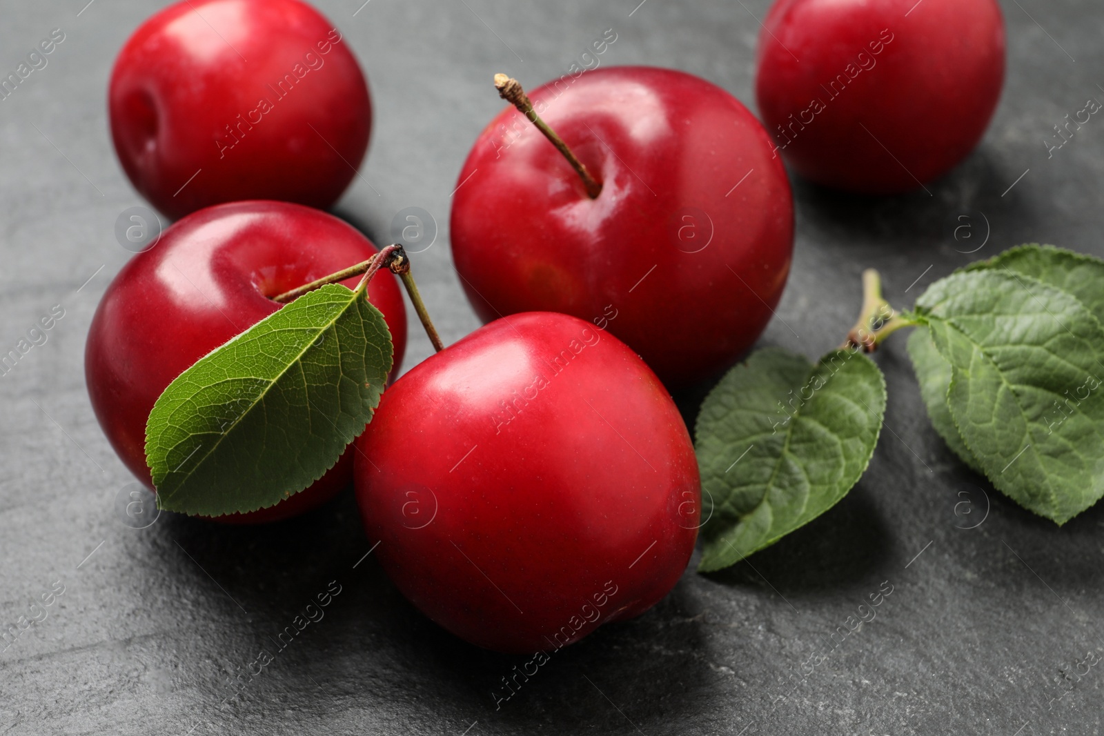 Photo of Delicious ripe cherry plums with leaves on black table, closeup