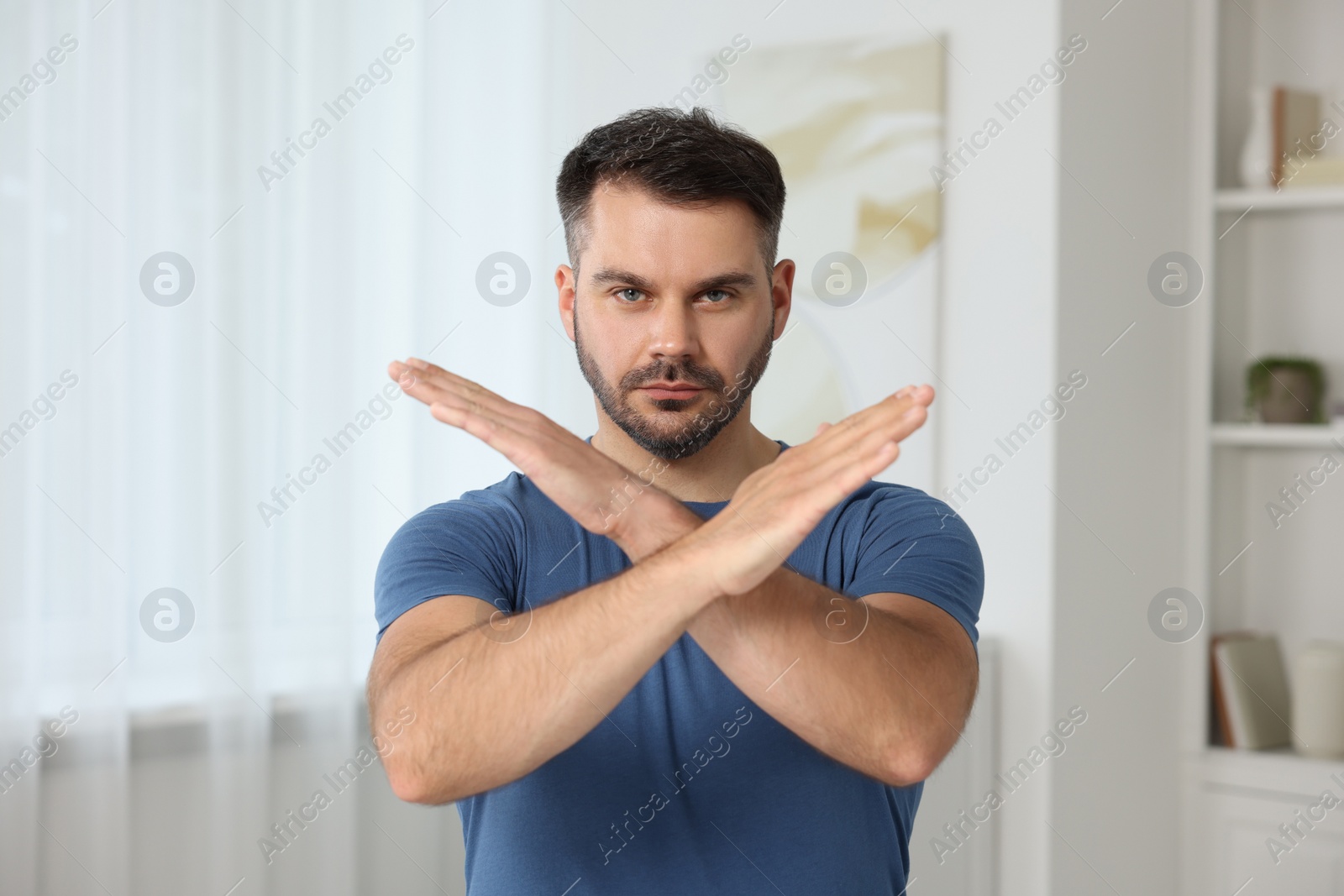 Photo of Handsome man with crossed hands at home. Stop gesture
