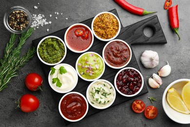 Photo of Different tasty sauces in bowls and ingredients on grey table, flat lay