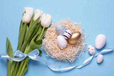 Photo of Many painted Easter eggs, tulip flowers and ribbon on light blue background, flat lay