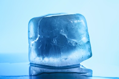 Photo of One crystal clear ice cube on light blue background, closeup. Color tone effect
