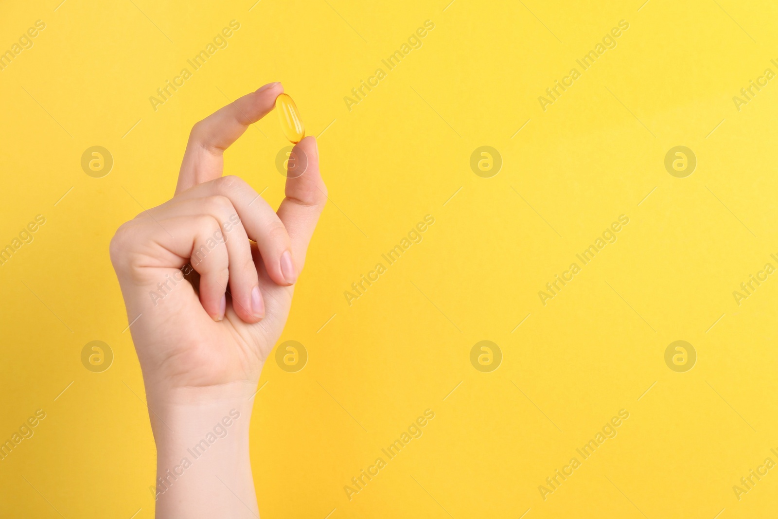 Photo of Woman holding vitamin capsule on yellow background, closeup. Space for text