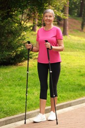 Photo of Happy senior woman performing Nordic walking outdoors