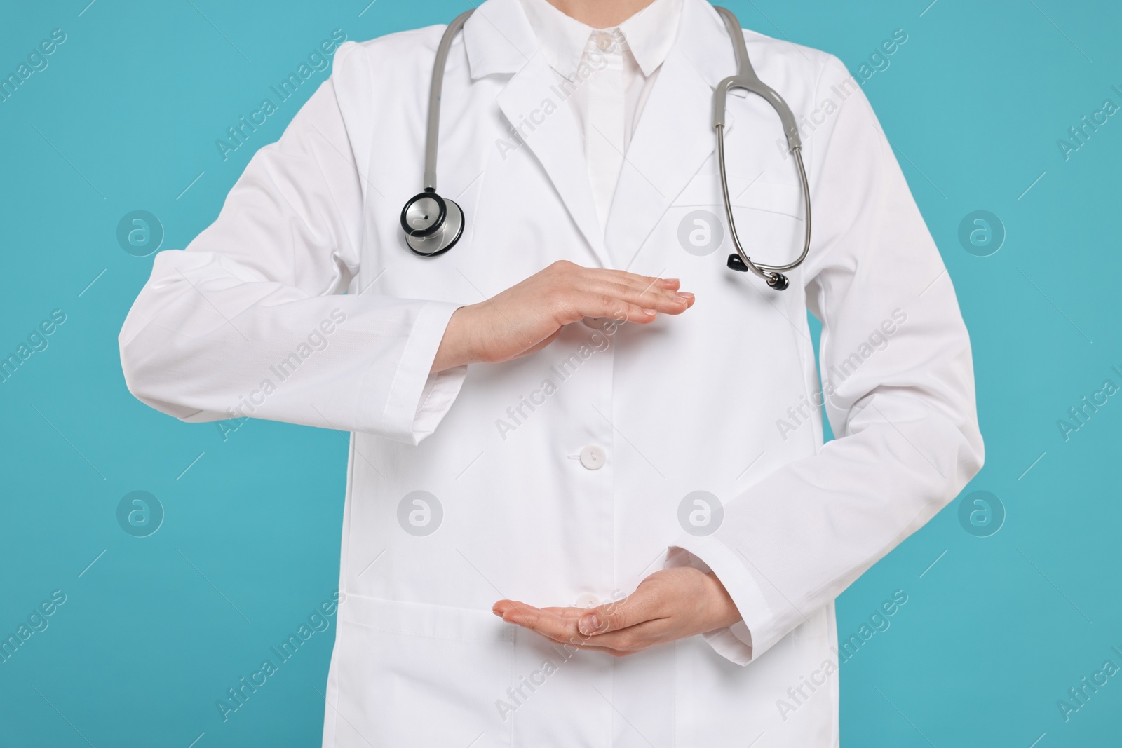 Photo of Doctor with stethoscope holding something on light blue background, closeup