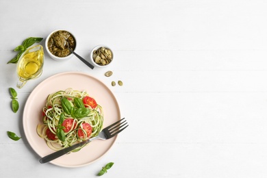 Photo of Delicious zucchini pasta with basil and cherry tomatoes served on white wooden table, flat lay. Space for text