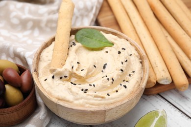 Delicious hummus with grissini sticks served on white wooden table, closeup