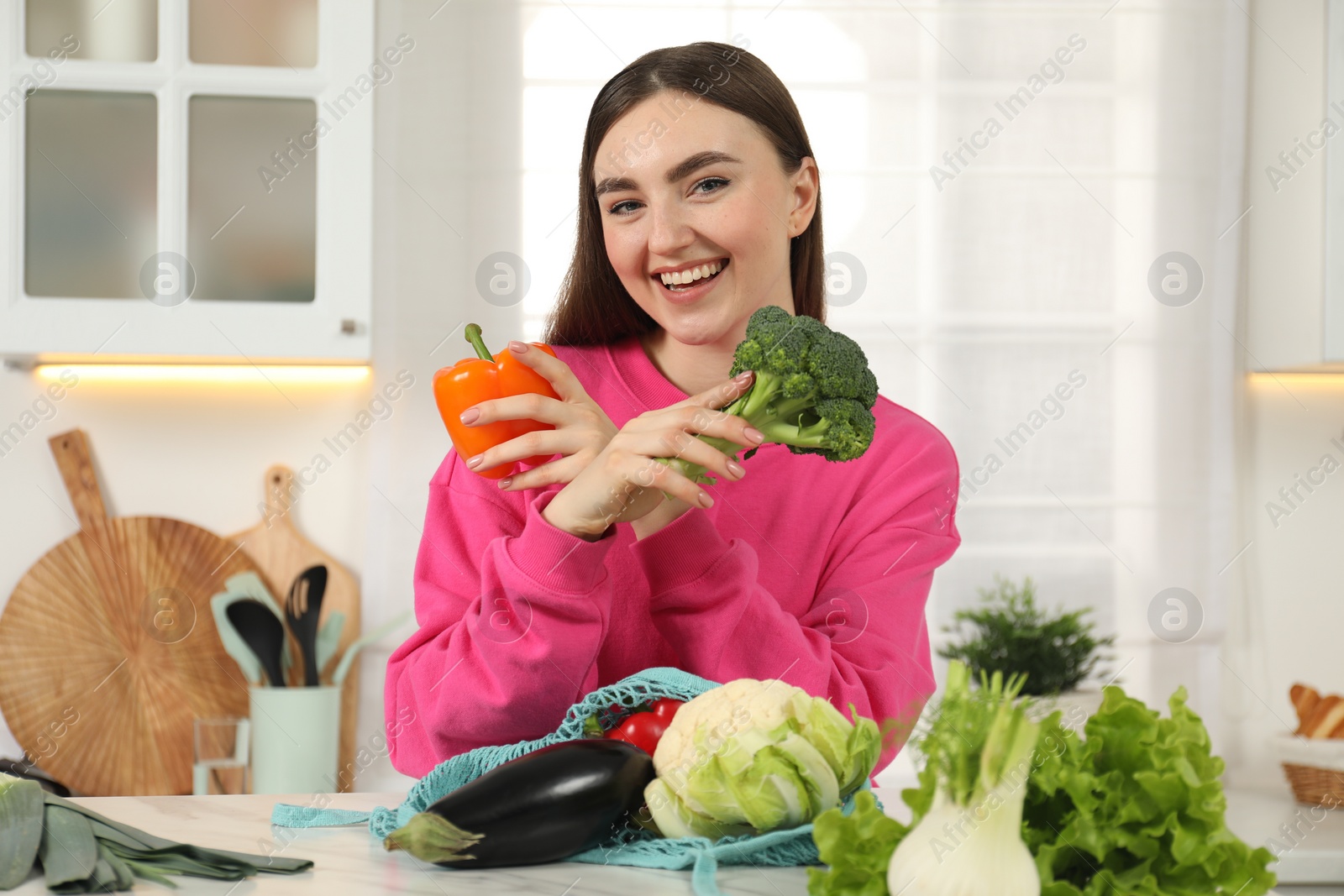 Photo of Woman with vegetables and string bag at light marble table in kitchen
