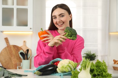Photo of Woman with vegetables and string bag at light marble table in kitchen