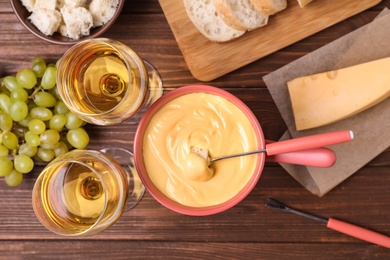 Flat lay composition with pot of cheese fondue and wine on wooden table