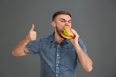 Young man eating tasty burger on grey background