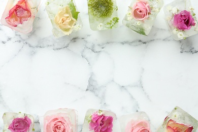 Ice cubes with flowers on marble background, flat lay. Space for text