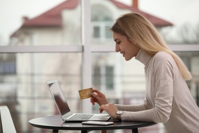 Photo of Woman with credit card using laptop for online shopping indoors