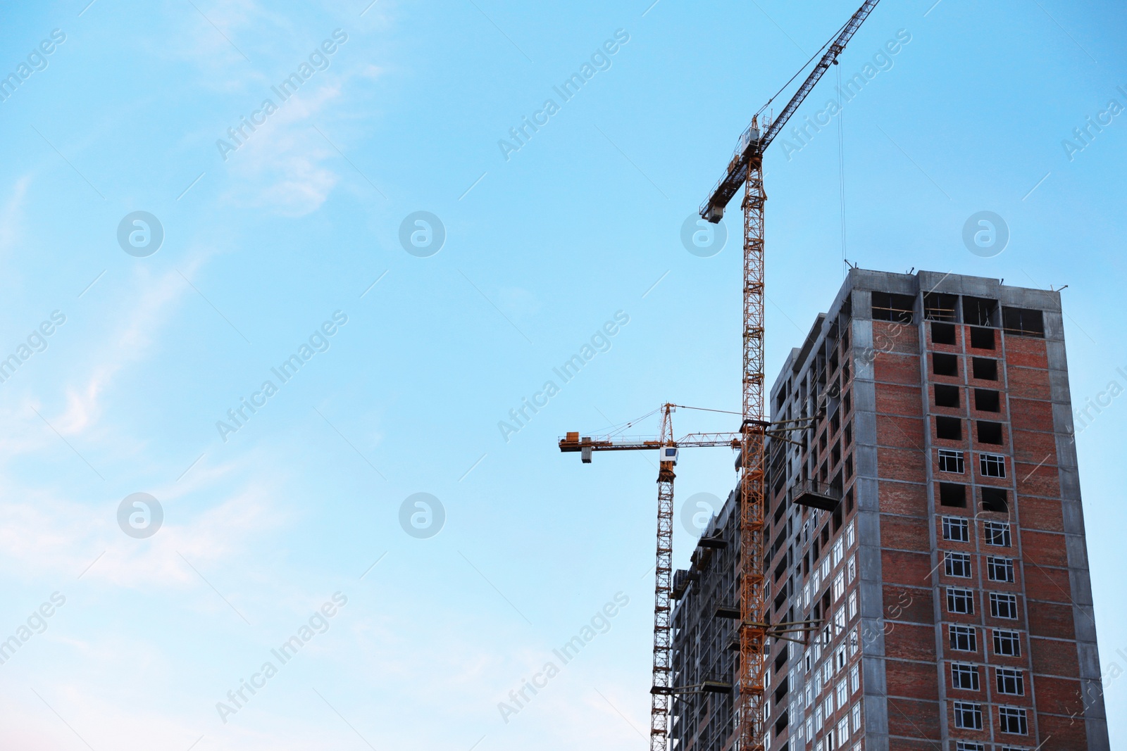 Photo of Construction crane and unfinished building against blue sky. Space for text