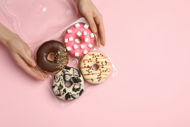 Photo of Woman with box of delicious donuts on pink background, top view. Space for text
