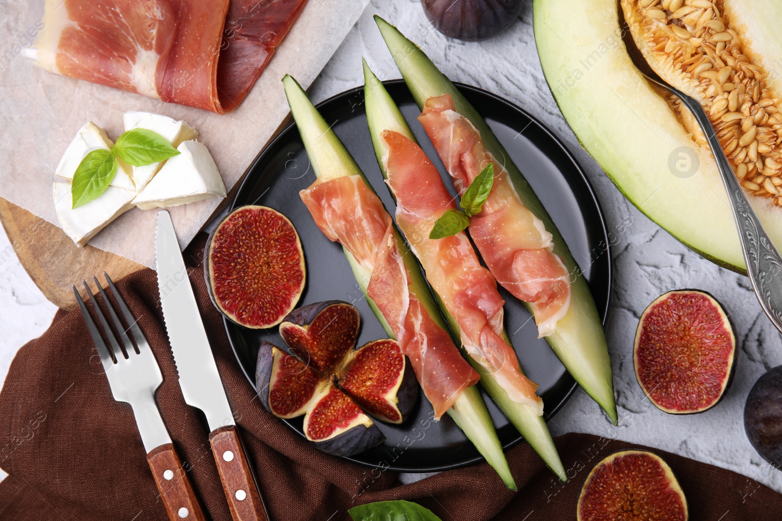 Photo of Tasty melon, jamon and figs served on white textured table, flat lay