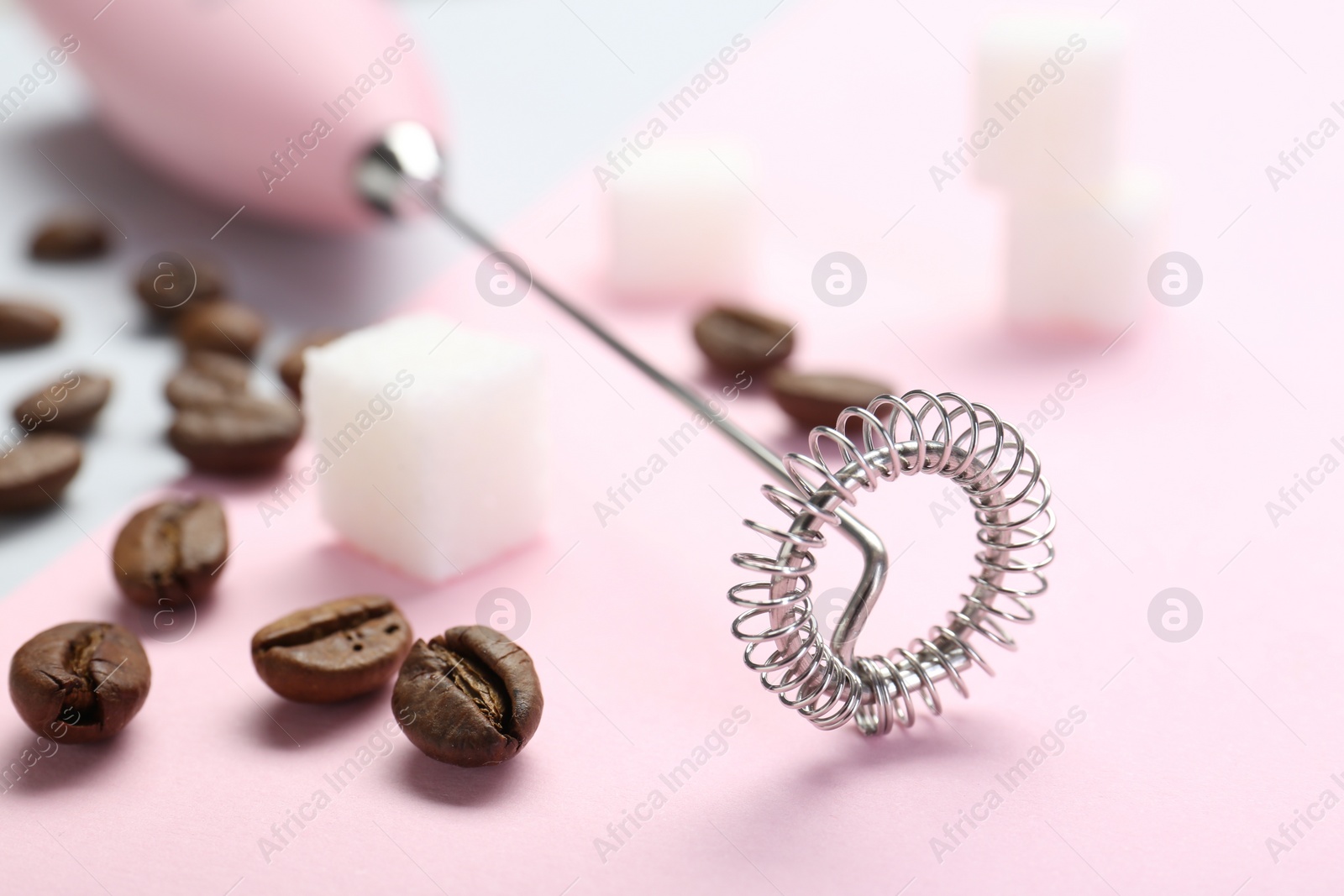 Photo of Pink milk frother wand, coffee beans and sugar cubes on color background, closeup