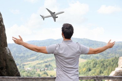 Image of Man looking at airplane flying in sky over mountains, back view