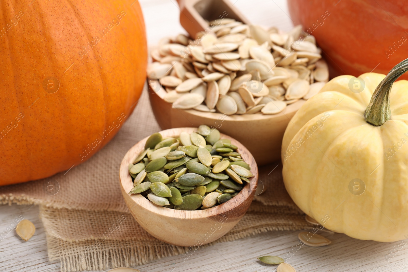 Photo of Bowls with seeds and fresh pumpkins on light wooden table