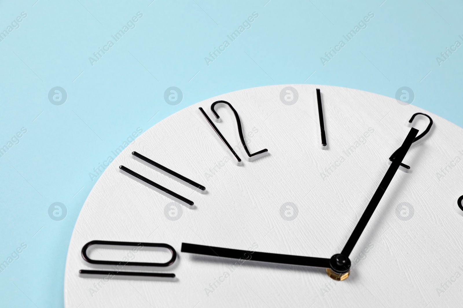 Photo of Stylish analog clock on light blue background, closeup