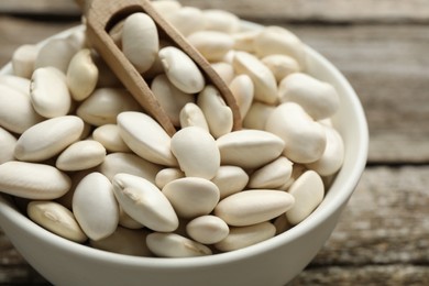 Bowl and scoop with uncooked white beans on wooden table, closeup