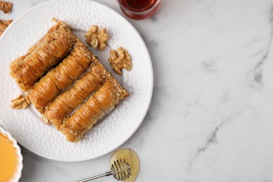 Photo of Eastern sweets. Pieces of tasty baklava, walnuts and tea on white marble table, flat lay. Space for text