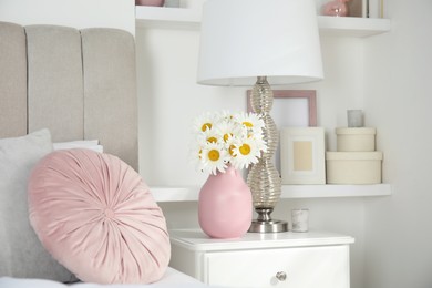 Photo of Bouquet of beautiful daisy flowers and lamp on nightstand in bedroom