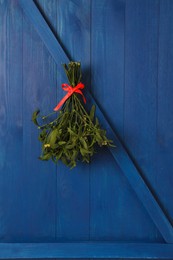 Photo of Mistletoe bunch with red bow hanging on blue wooden wall. Traditional Christmas decor