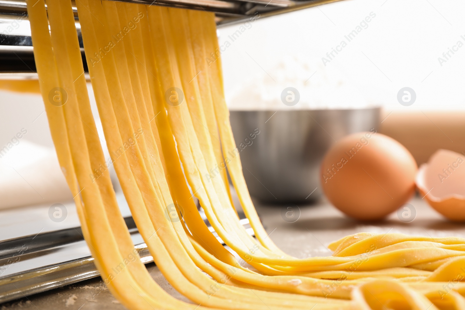 Photo of Pasta maker machine with dough on grey table, closeup