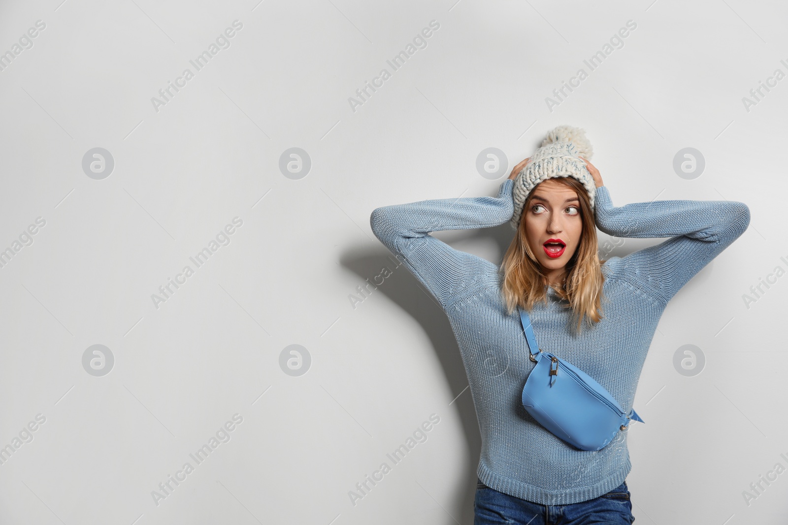 Photo of Emotional young woman in warm sweater with bag on white background. Space for text