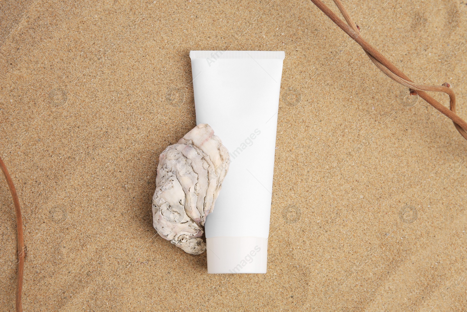 Photo of Tube with cream, shell and branches on sand, top view. Cosmetic product