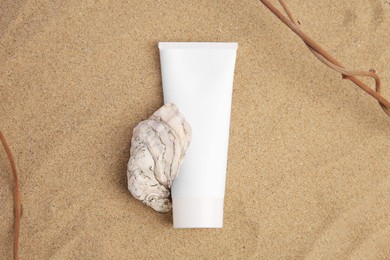 Tube with cream, shell and branches on sand, top view. Cosmetic product