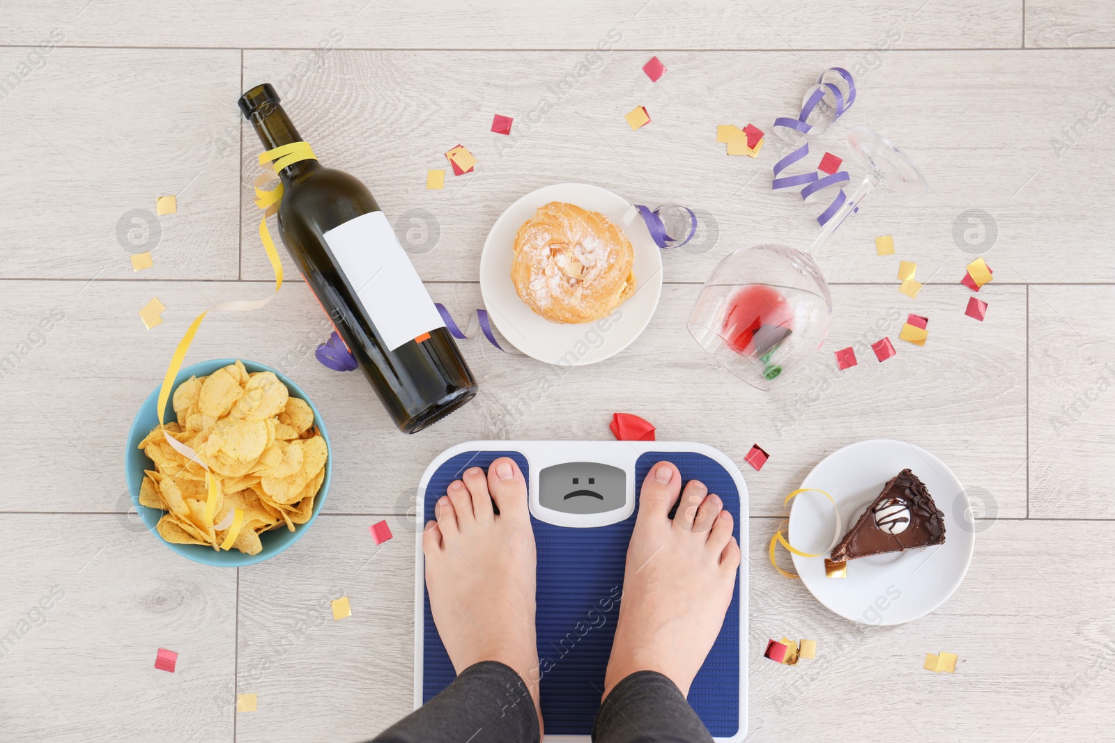 Photo of Woman standing on scales surrounded by different food and alcohol after party indoors, top view