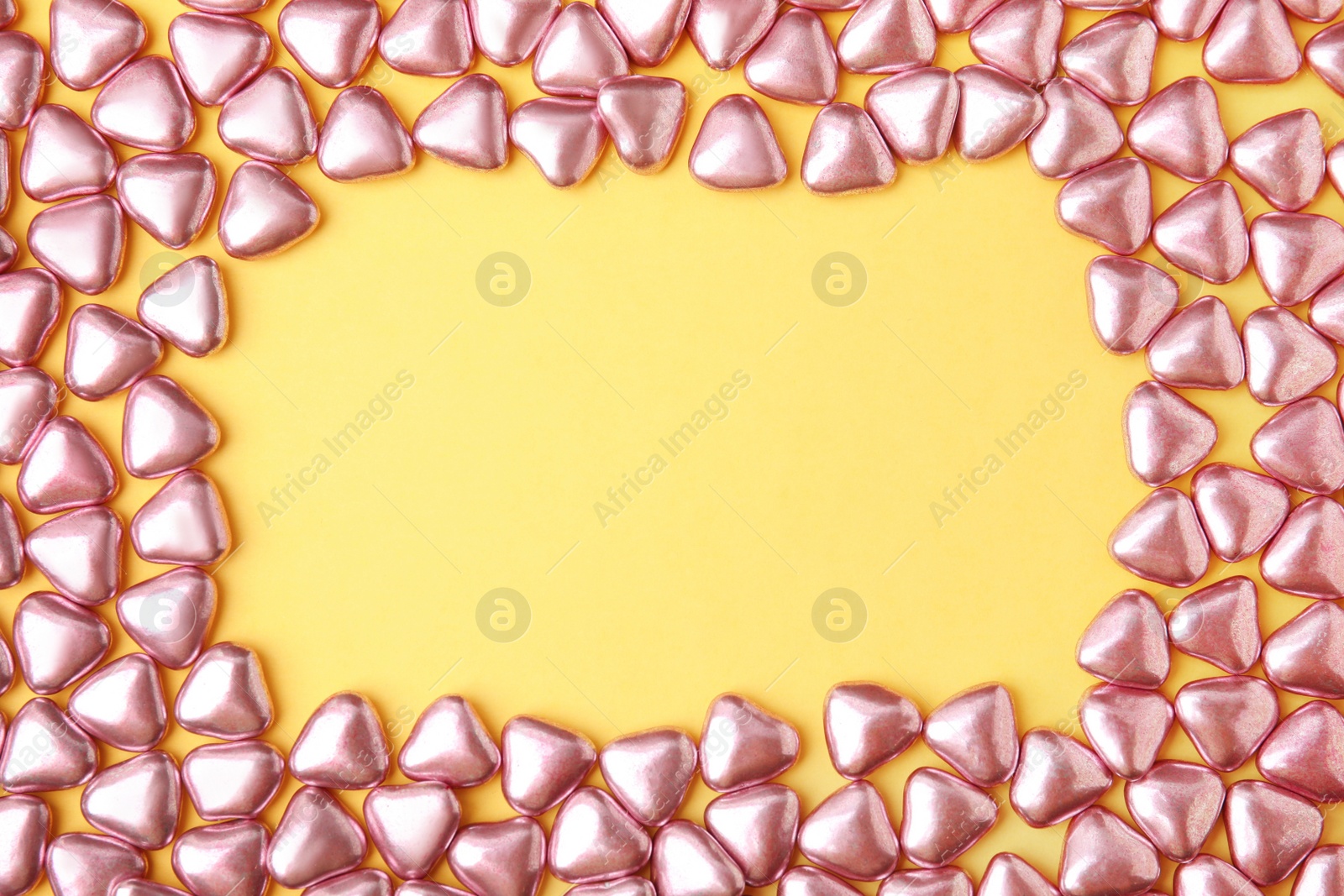 Photo of Frame made of delicious heart shaped candies on yellow background, flat lay. Space for text