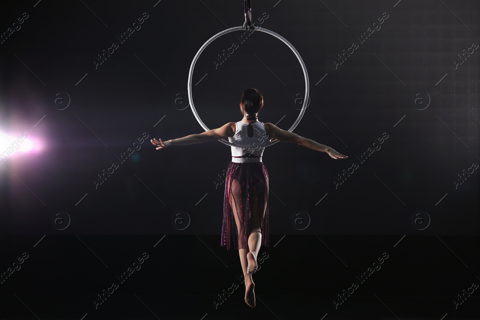 Photo of Young woman performing acrobatic element on aerial ring against dark background