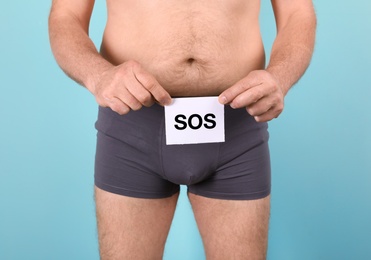 Senior man with urological problems holding SOS sign on color background