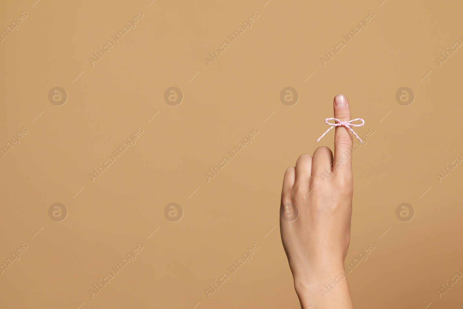 Photo of Woman showing index finger with tied bow as reminder on light brown background, closeup. Space for text