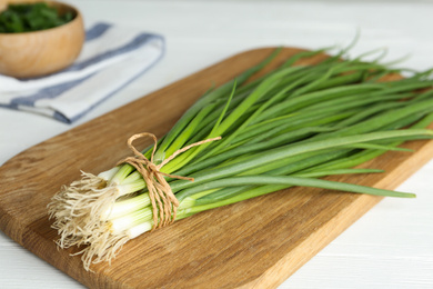 Photo of Fresh green spring onions on wooden board, closeup