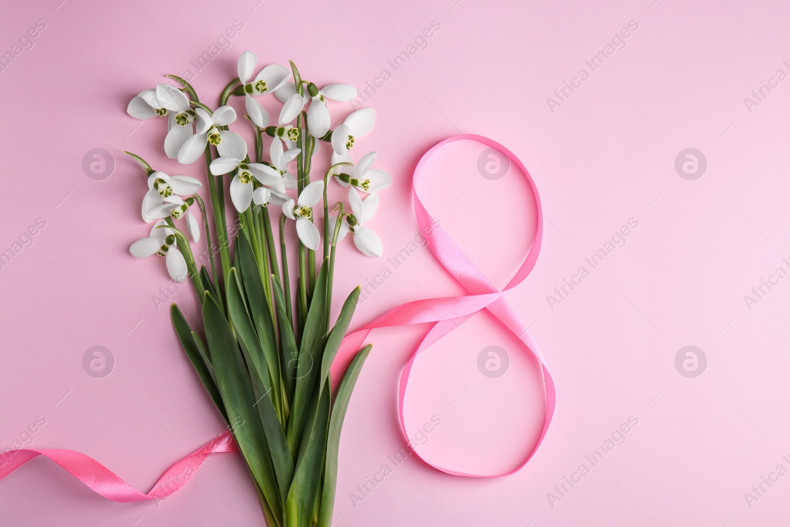 Photo of Beautiful snowdrops and number 8 made of ribbon on pink background, flat lay