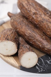 Whole and cut cassava roots on white table, closeup